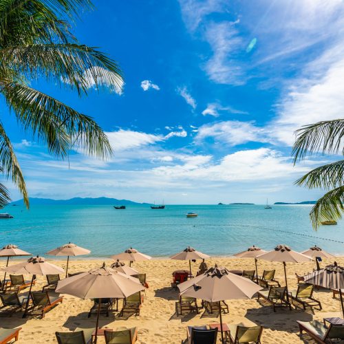 Beautiful tropical beach sea and ocean with coconut palm tree  and umbrella and chair on blue sky and white cloud for holiday vacation travel